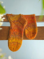 Pair of orange and yellow handknitted socks on a wooden chair with a blurred natural background