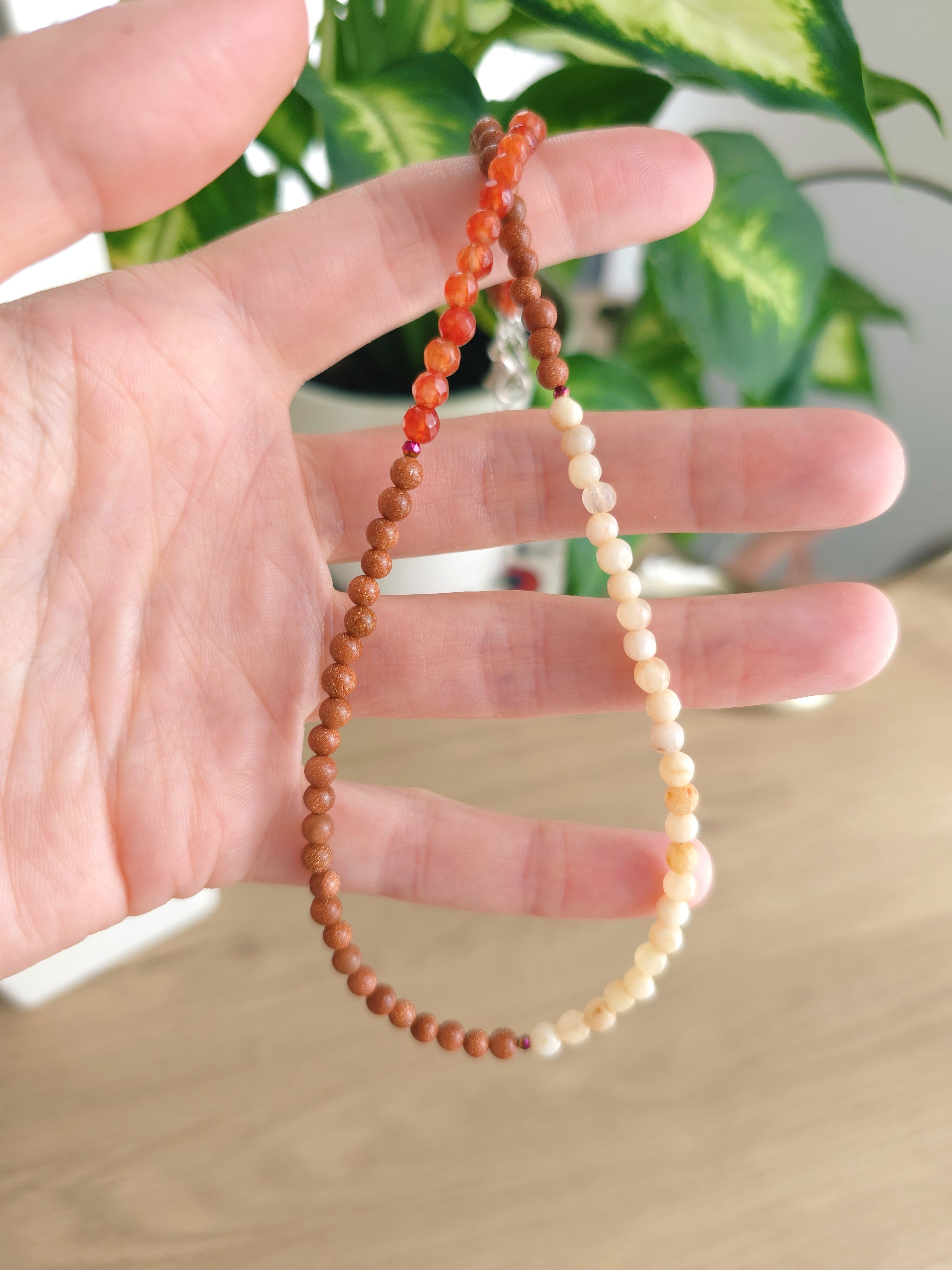 Kaklarota no oranžiem, brūniem un bēšiem dabīgajiem akmeņiem. Tieva kreļļu virtene sievietēm ar dīfenbahiju fonā. 