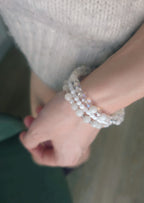 Close-up of a wrist wearing multiple beaded white bracelets with a blurred background