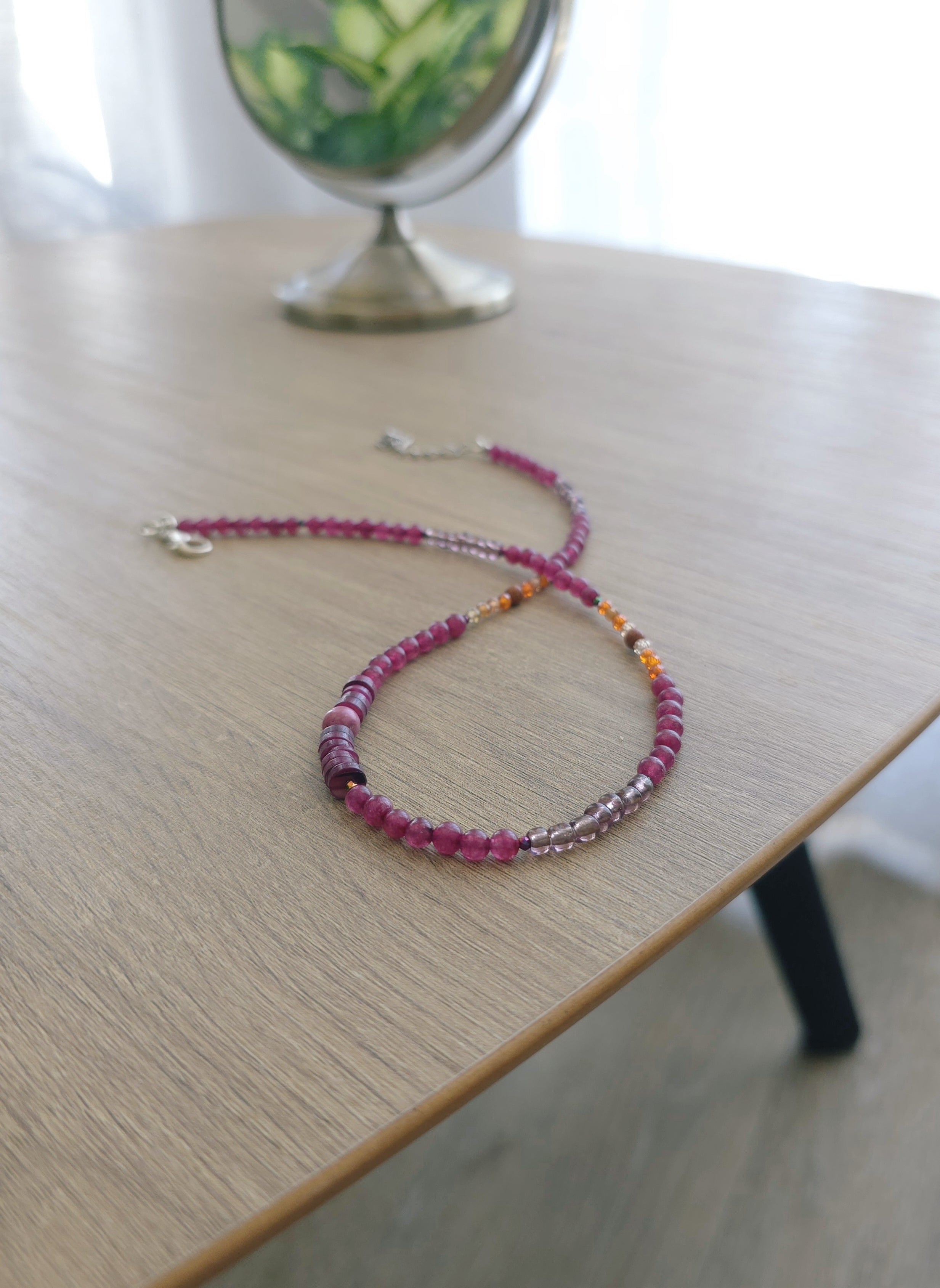 Blāvi rozā eleganta kaklarota sievietēm. Spugulis un krelles uz kafijas galdiņā. 