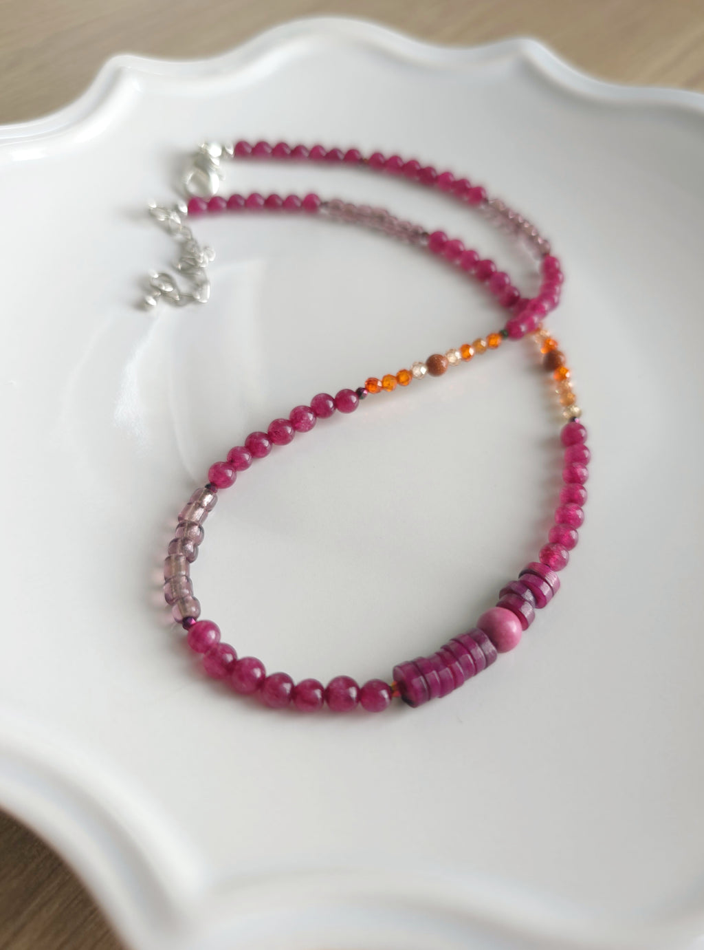 beaded adjustable necklace with pink and orange beads on a white dish.