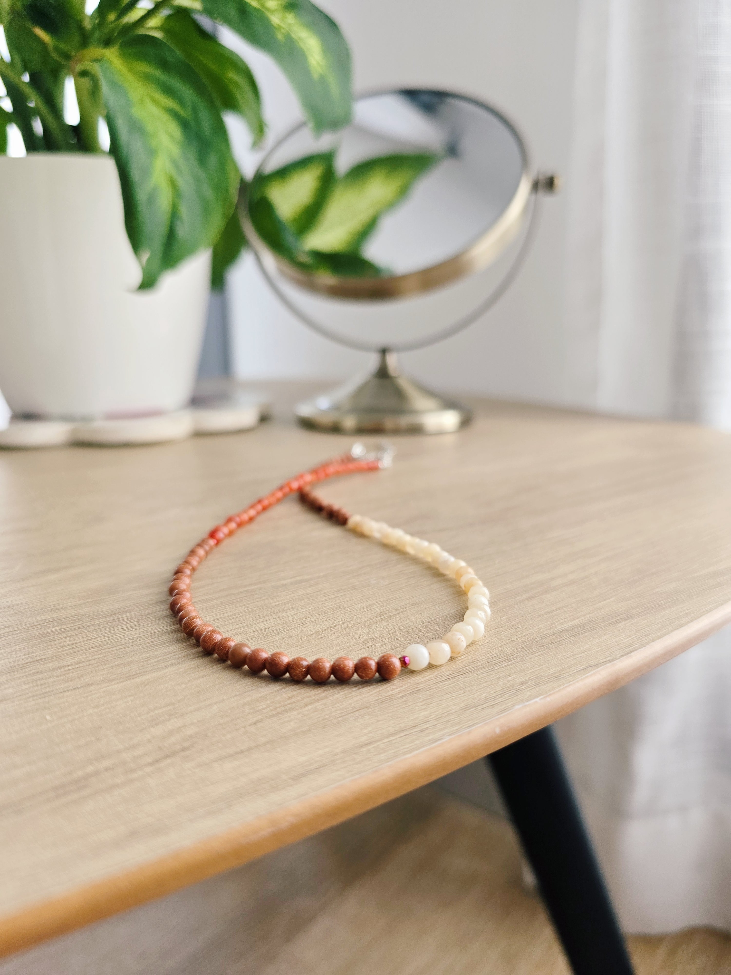 Tricolor necklace on a beige wooden coffee table with a plant and mirror from Leroy Merlin in the background