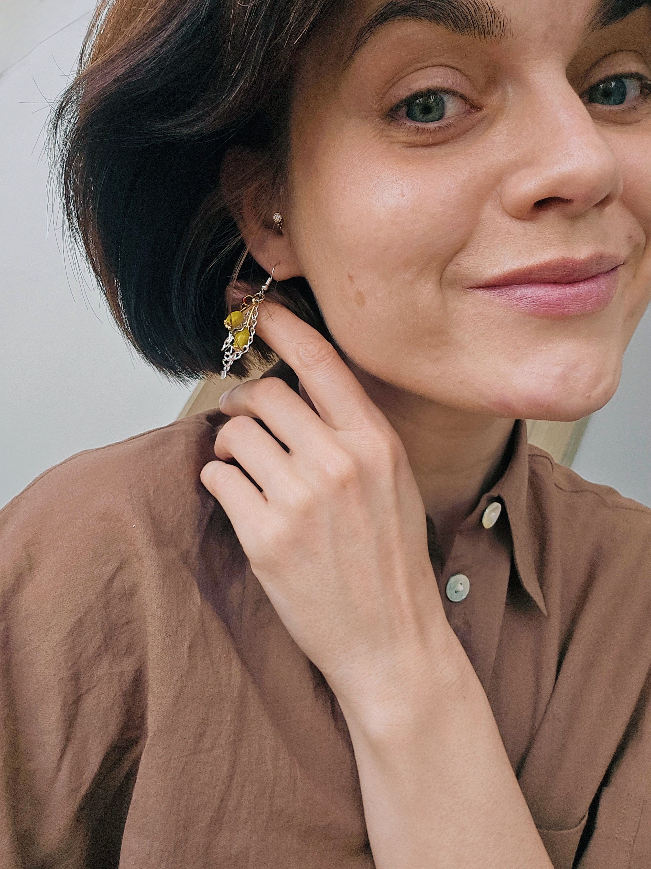 Woman in brown classy Zara shirt wearing a yellow tulip earring, touching her ear with a neutral background